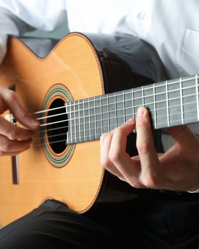 Man playing on classic guitar against light background, space for text Man playing on classic guitar against light background, space for text